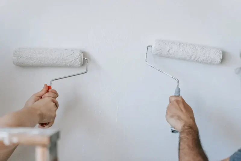 Two painters applying white paint to an interior wall