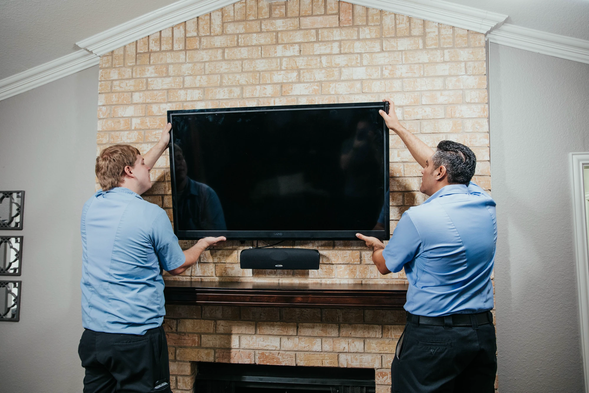 Two Hank's technicians mounting a television above a brick fireplace