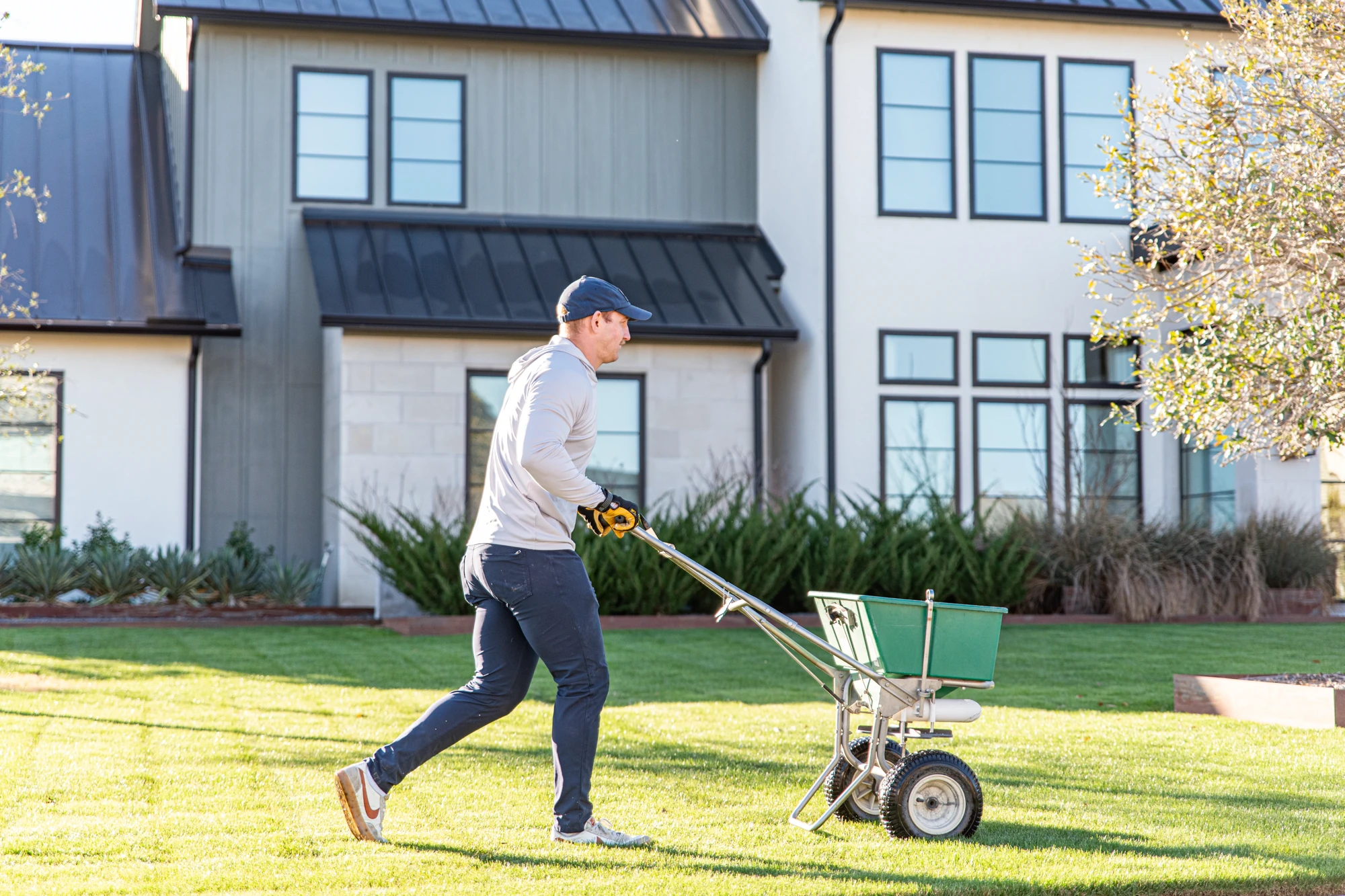 Lawn care technician pushing a broadcast spreader across a yard