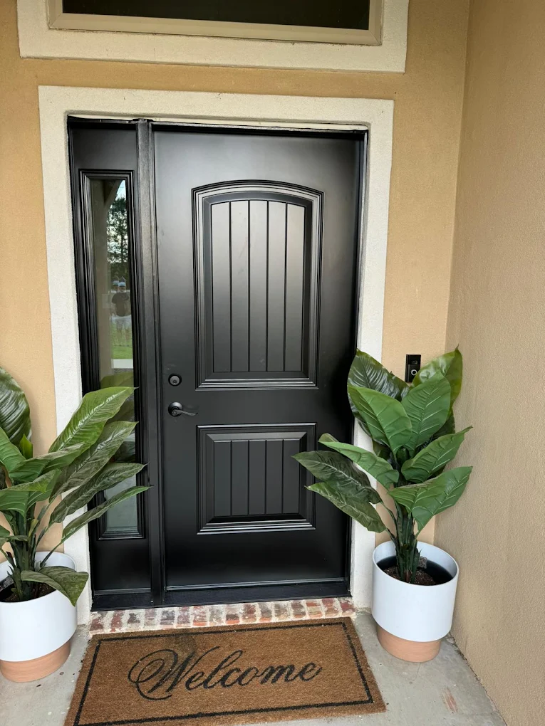 Black front door styled with plants and a welcome mat